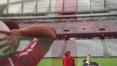 Kırmızı formalı atıcı bileklerini kırıyor, topu ragbi çizgisine fırlatıyor, yay yolu gösteriyor. Atletizm, takım çalışması, rekabet, strateji, stadyum, sportmenlik, aksiyon