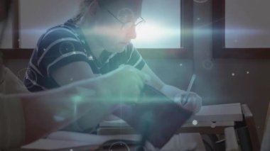 Sınıf arkadaşının yanında not yazan öğrenci kalem çekerek masalar arasında ders vermeye başlıyor. Eğitim, işbirliği, teknoloji, yenilik, odaklanma, öğrenme, sınıf