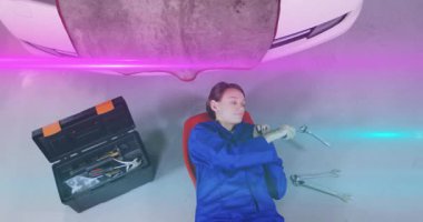 Otomotiv teknisyeninin alet çantasına bakması, İngiliz anahtarını tutması, yükseltilmiş şasinin altındaki cıvatayı sıkması. Tamirat, atölye, aletler, onarım, sanayi, işçilik, bakım