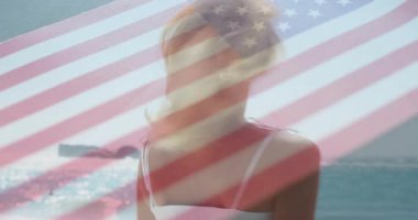 Kameraya bakan, kumsala dönen, saçları süpüren şeffaf bayrak kaplayan bir kadın. Sahil, sahil, yaz, kadınlık, özgürlük, yaşam tarzı, sükunet