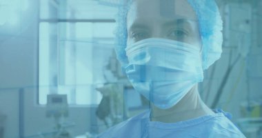 Mavi cüppeli, maskeli ve kabarık şapkalı bir cerrah ameliyathanede camların arkasında monitörlerle bekliyor. Tıbbi, steril, sağlık, kesinlik, teknoloji, profesyonel, klinik