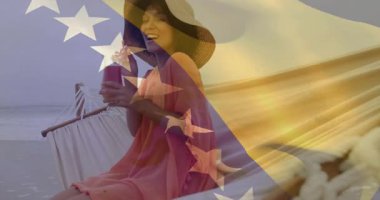 Kumsalda hamakta uzanan kadın turizm için dalgalanan şeffaf bayrağın ardından kokteyl yudumluyor. Plaj, tatil, dinlenme, gün batımı, eğlence, kutlama, tropikal