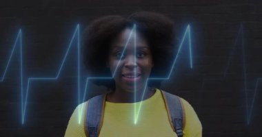 Sarı kazak ve sırt çantası giyen bir kadın, kalp atışları göğsüne doğru yükselirken gülümsüyor. Dijital, sağlıklı, enerjik, teknoloji, sağlık, gençlik, güven