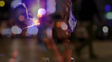 Şarkıcı mikrofonu kavrıyor ve hareketli Bokeh ışıkları eşliğinde sokak kalabalığı için şarkı söylüyor. Performans, gece hayatı, canlılık, enerji, sokak müziği, sahne aydınlatma, konser