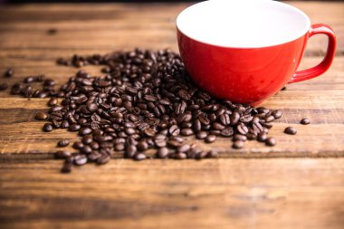 Düz dizayn kırmızı seramik bardak ön planda dağınık kahve çekirdekleri ile ahşap masanın üzerinde duruyor. Seramik, kırsal, sıcak, kahve, içecek, kafe, el yapımı