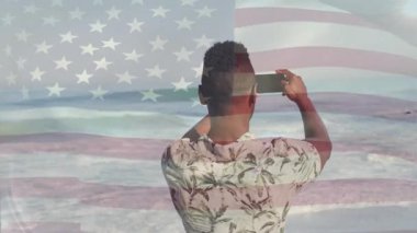 Dijital pazarlamacı, telefon yönlendirme yöntemlerini kullanarak okyanusa bakıyor, bayrak kaplamalı dalgaları kaydediyor. Sahil, sahil, okyanus, dalgalar, sahil, sükunet, macera