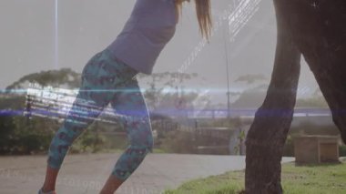 Destek için ağaç gövdesine yaslanan bir kadın, fitness teknolojisi kaplamasında zayıflıyor. Açık hava, sağlık, esneklik, dijital arayüz, doğal, zindelik, sağlık