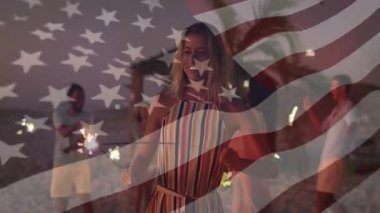 Plaj arkadaşı olan bir kadın maytap grubuna adım atıyor ve fitil ışığında kıvılcımlar sallıyor. Kutlama, dostluk, alacakaranlık, sahil kenarı, ışıltı, boş zaman, samimiyet.