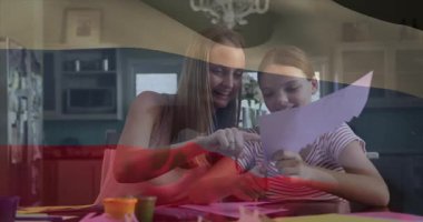 Anne kağıda doğru eğiliyor, kız el işi sırasında animasyon rehberi boyunca kağıt kesiyor. Aile, takım çalışması, yaratıcılık, diy, çocukluk, bağ, kırsal