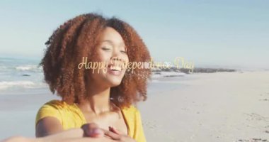 Partnerin elini tutan kadın kamerayı çekiyor ve Bağımsızlık Günü mesajı ile plajda dönüyor. Neşeli, neşeli, canlı, açık hava, boş zaman, birliktelik, yaşam tarzı.