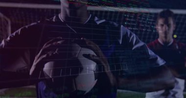 Top yakalayan ve oyun analizlerini etkinleştiren ön oyuncu takım arkadaşı izlerken istatistikleri takip ediyor. Futbol, analitik, performans, teknoloji, spor bilimi, stadyum, takım çalışması