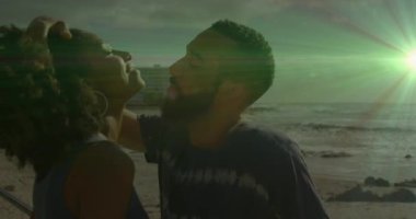 Saçlarını tarayan adam gün batımında kayalık okyanus kıyısında öpüşen çift seyahat romantizmi gösteriyor. Romantizm, samimiyet, bağlantı, dinginlik, çift, manzara, doğal