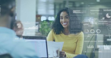 Woman in yellow top analyzing report with data overlays at modern open-plan office, with laptop. Business, teamwork, innovation, professional, collaboration, digital, analytics