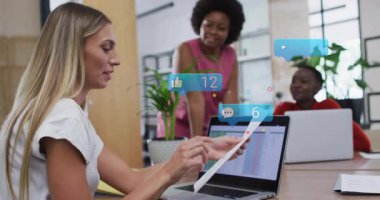 Blonde iş arkadaşı rapor seçiyor ve laptopa verileri işaret ediyor, farklı sosyal simgeler. İşbirliği, takım çalışması, veri analizi, modern çalışma alanı, dijital bağlantı, mesleki gelişim, ofis ortamı