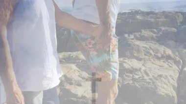 Kıdemli bir kadın partnerin elini tutuyor ve pürüzlü kayalara basıyor. Sağlık haçı dalgaları örtüyor. Macera, arkadaşlık, canlılık, takım çalışması, açık hava, kıyı, huzur