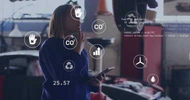 Garajdaki kadın teknisyen akıllı telefonu kaldırırken karbondioksit ikonlarının emisyon verileri için tablet aşırdığını gösteriyor. Teknisyen, tanı, sürdürülebilirlik, yenilik, dijital, teknoloji, otomotiv.