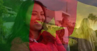 Şeffaf Kamerun bayrağı soluyor ve arkadaşlarını gün batımında çatıda sosyalleşirken gösteriyor. Arkadaşlık, sosyalleşme, günbatımı, şehir, eğlence, doğa, canlı