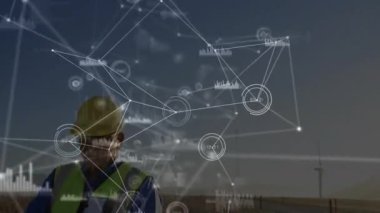 Saha teknisyeni dinleme cihazı ve şeffaf veri örtüleriyle rüzgar çiftliği performansını izliyor. Yenilenebilir, teknoloji, analitik, sürdürülebilirlik, yenilik, sanayi, dijital