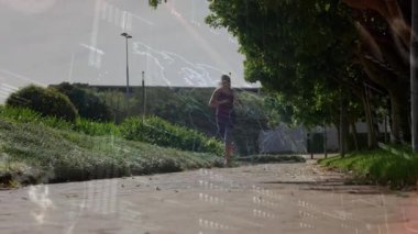 Kadın koşucu kameraya yaklaşıyor, güneşli kentsel yeşil yolda animasyon fitness haritasını etkinleştiriyor. Fitness, outdoor, dynamic, modern, technology, health, activewear