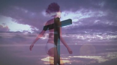 Günbatımında ahşap haçın arkasından yürüyen manken kayan gökyüzüne karşı beyaz mayo gösteriyor. Siluet, günbatımı, açık hava, kumaş, sükunet, bohem, canlı