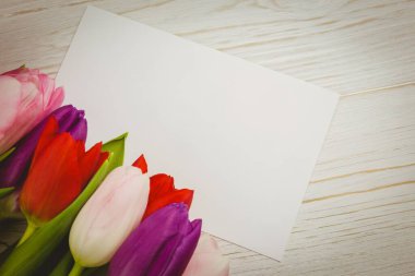 Düz dizayn, boş beyaz tebrik kartı ahşap masanın üzerinde duruyor, lalelerle, kopyalama alanıyla. Kırtasiye, çiçek, minimalizm, davetiyeler, doğa, zarafet, tasarım