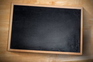 Çerçevelenmiş karatahta, ahşap masa üstünde, yumuşak yukarıdaki ışığın altında köşegen olarak duruyor. Sanatçılık, minimalizm, doğal, doku, iç mekan, eğitim, zarafet