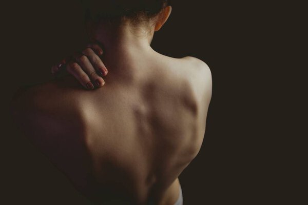 Женская голая спина и плечи светятся в студии, снятой под мягким светом на тёмном фоне. Искусство, искусство, минимализм, красота, проницательность, уязвимость, контраст