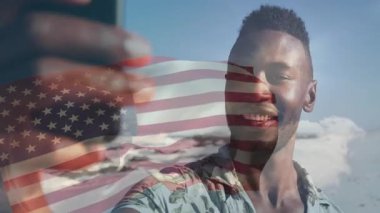 Adam güneşli sahilde seyahat selfie 'si çalarken telefon panjuruna basıyor ve soluk Amerikan bayrağı kaplıyor. Macera, tatil, boş zaman, açık hava, dingin, canlı, keşif
