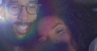 Renkli ışık altında eğilen çift mercekle gülüyor ve pazarlama içeriği yaratıyor. Sevgi, bağlantı, neşe, samimiyet, portre, canlı, yaratıcı