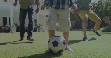 Çocuk spor antrenmanında futbol topuna vuruyor, baba ve büyükbaba onu sahada kovalıyor. Aile, aktivite, açık hava, neşeli, gündelik, güneş ışığı, bağlantı