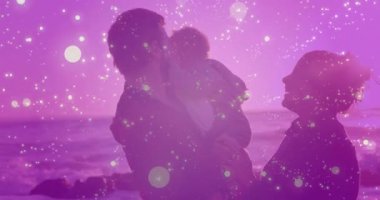 Baba, anneye doğru bebeği kaldırıyor ve gün batımında ebeveynlik için kıvılcımların arasında bebeği öpüyor. Aile, şefkat, yakınlık, sahil, sükunet, bağlantı, kutlama