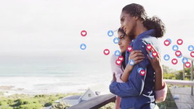 Anne ve kızı balkonda okyanusa bakarken sosyal medya simgeleri destek veriyor. Aile, bağlantı, doğa, sükunet, huzur, şefkat, uyum.