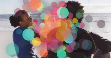 Smiling adult friends wearing wetsuits holding two surfboards on sunlit sandy beach. Vibrant, energetic, adventure, friendship, outdoor, leisure, summer
