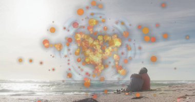 Sitting elderly couple in colorful jackets on ocean beach, with orange digital overlay, copy space. Seaside, companionship, relaxation, data visualization, tranquility, leisure, technology