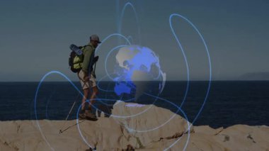 Bir adam yürüyüş direkleri dikiyor ve kıyı kayalıklarına tırmanıyor. Yerküre haritası eşleştirme güzergahıyla. Macera, keşif, vahşi doğa, engebeli, açık hava, yolculuk, teknoloji