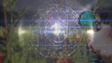 Bahçıvan, bitki verilerini gösteren dijital ağ küresini atarken domatesleri spreyleyen başlığa basıyor. Bahçecilik, teknoloji, dijital, sürdürülebilirlik, açık hava, yenilik, bağlantı