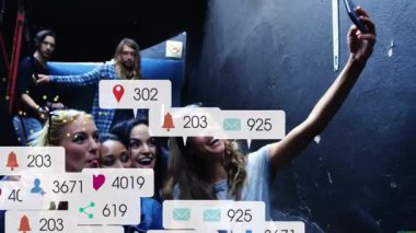 Arkadaşları merdiven boşluğunda selfie çekmek için telefon açıyor yüzen sosyal medya ve Bitcoin ikonları üretiyor. İşbirliği, kutlama, teknoloji, şehir, canlı, dinamik, bağlantı