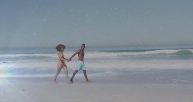 Soldan gelen çift, güneşli sahil şeridinde el ele yürürken, güneş ışığı turizmi canlandırıyor. Romantizm, deniz kenarı, eğlence, canlılık, uyum, yaz, açık hava