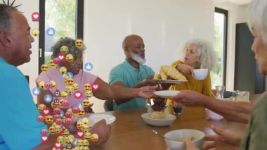 Yetişkin grup tabakları uzatıyor ve kahve yudumluyor. Sosyal medya emojileri masada yükseliyor. Sosyal toplanma, aile toplantısı, toplu yemek, gündelik kutlama, samimi etkileşim, modern iç mekan, canlı ruh hali.