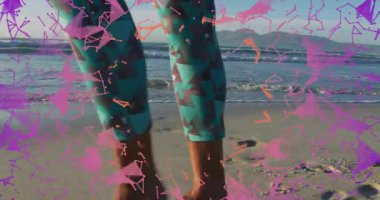 Kıdemli bir kadın ıslak kuma basıyor, sağlık örtüsü oluşturuyor, desenli tozluklarda yürüyüşü analiz ediyor. Sağlık, hareket, dinginlik, biyomekanik, açık hava, enerjik, estetik