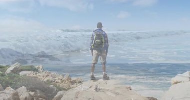 Kayalık deniz manzarası gördükten sonra kollarını kaldıran erkek yürüyüşçü çarpan dalgalarla sağlığı destekliyor. Macera, sağlık, keşif, doğa, manzara, açık hava, ilham