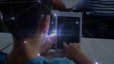 Öğrenci masadaki tableti alıp ekrana dokunuyor ve parlayan ağ örtüsü oluşturuyor. Teknoloji, etkileşim, dijital, bağlantı, yenilik, eğitim, fütüristik