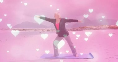 Kumsalda yoga minderine basan bir kadın. Elinde savaşçı II 'nin yüzen kalpleriyle sağlık pozu var. Spor, sağlık, meditasyon, dinginlik, farkındalık, açık hava, rahatlama.