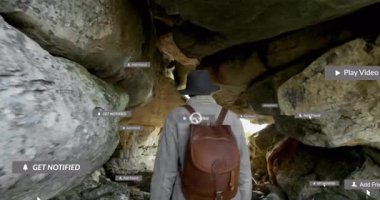 Keşif aracı kayalık mağara girişini gözetliyor, teknolojik uyarıları etkinleştiriyor ve gözlemlemek için dürbünü alıyor. Macera, keşif, gezinme, yaban hayat, teknoloji, keşif, engebeli