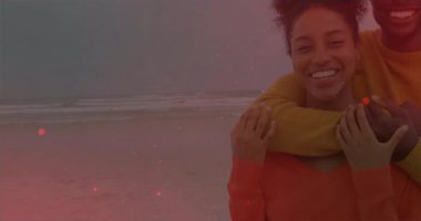 Bulutlu sahilde kadının kollarına sarılan bir adam seyahat pazarlaması için canlandırılmış kalp simgelerini aktifleştiriyor. Romantizm, şefkat, bağlantı, mutluluk, eğlence, açık hava, yaşam tarzı