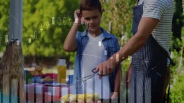 Baba ızgara kapağını kaldırıp ızgara mısır ve sosis pişiriyor. Oğula maşa kullanıyor. Animasyon barbekü ısı göstergesi kullanıyor. Aile, açık hava, eğlence, ızgara, yerli, kutlama, kırsal