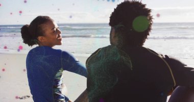 Dalgıç kıyafetli yetişkin bir çift sahilde dalgaların dalgalanmasını seyrediyor, güneşli bir gökyüzü. Macera, deniz, su, aktif giysi, keşif, boş zaman, sahil