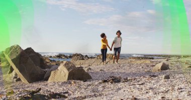 Yürüyen adam ve kadın kayalık kıyı şeridinde el ele tutuşuyorlar, çakıl taşları okyanus dalgalarıyla. Romantik, macera, manzara, sükunet, doğa, eğlence, bağlantı