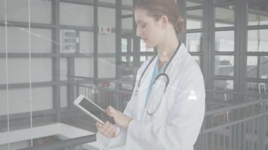 Kadın doktor atriyum yürüyüş yolunda tablet tıklatıyor, animasyon çizelgelerini etkinleştiriyor, sonra da tableti sokuyor. Tıbbi, teknoloji, sağlık, teletıp, profesyonel, yenilik, sağlık sektörü