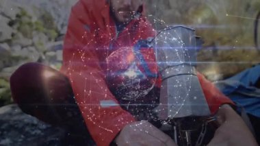 Kamp sobası açan ve kahve yakan bir adam. Teknoloji ağı küresiyle kaplanmış bir kahve. Macera, vahşi doğa, keşif, açık hava, engebeli, doğal, rahatlama.